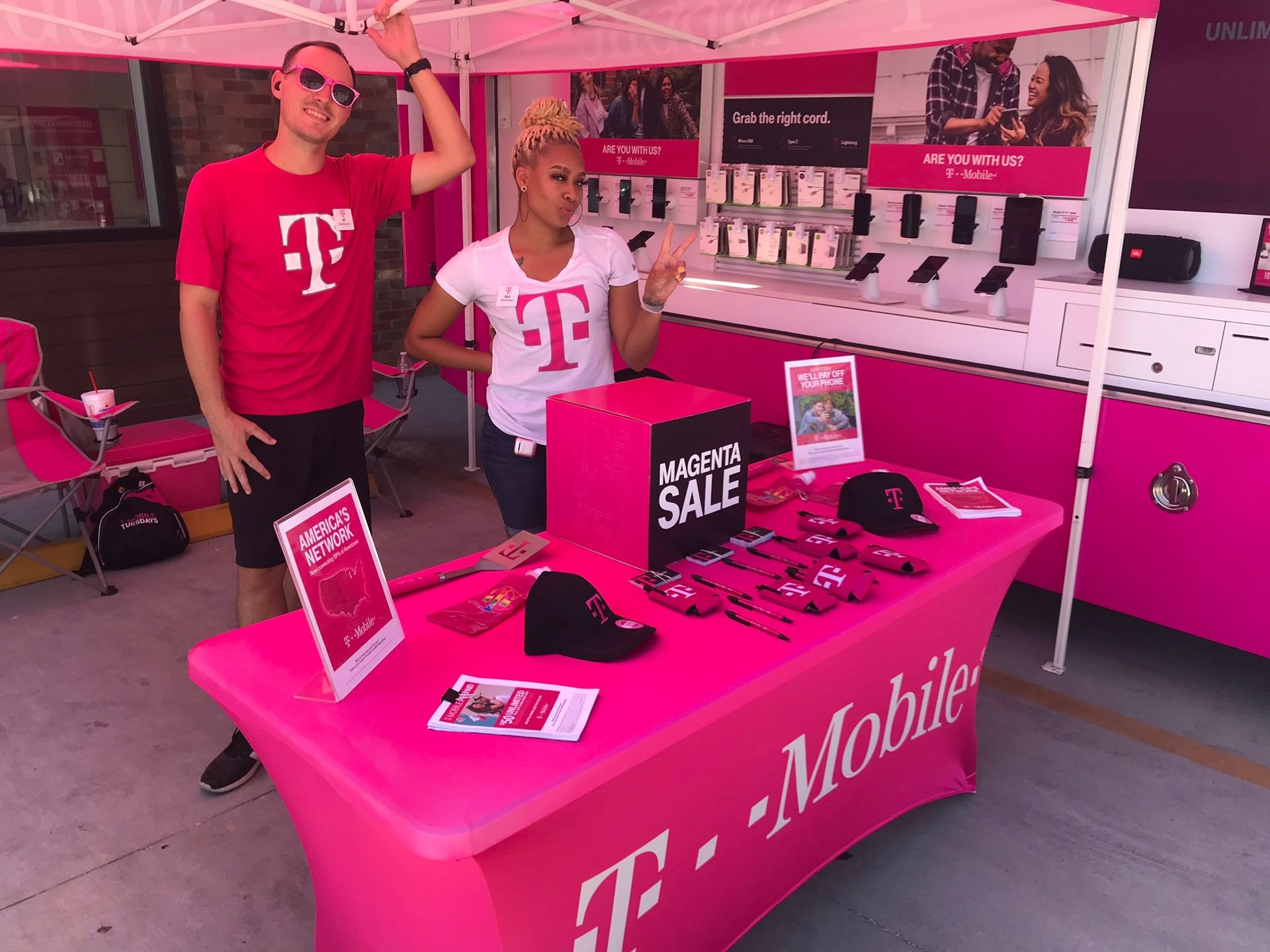 T-Mobile promotion booth with branded merchandise and signage, staffed by two individuals wearing T-Mobile shirts.